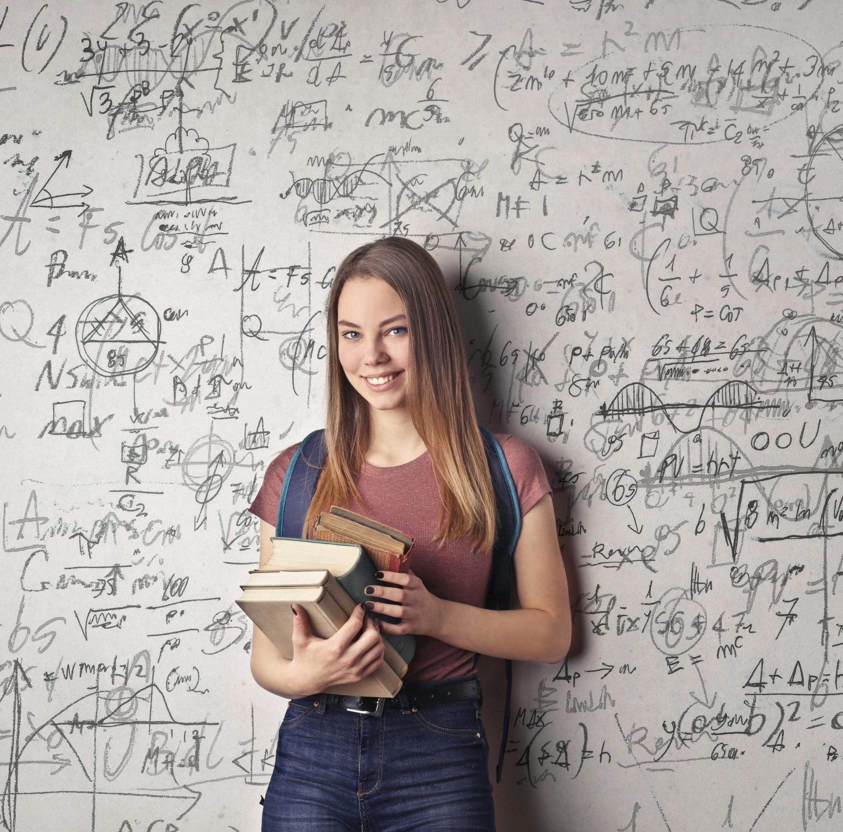 Young woman holding books standing in front of a chalkboard filled with mathematical formulas.